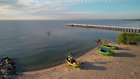 empty fisher boats on sandy beach by the gdynia orlowo pier molo, poland - aerial flyover at sunrise