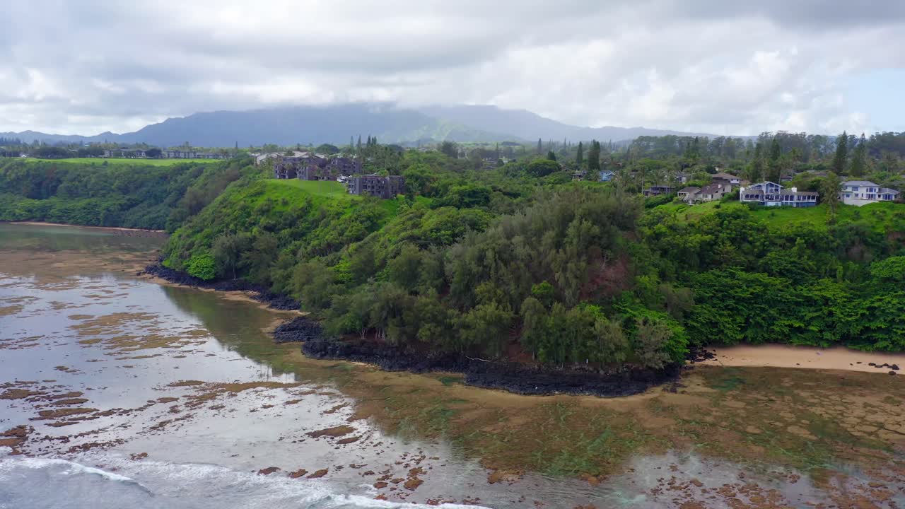 4K aerial of Sea Lodge Beach showing dark lava rock formations, bright coral reefs, and clear turquoise water. Natural textures and shallow depth highlight Kauai’s untouched shoreline
