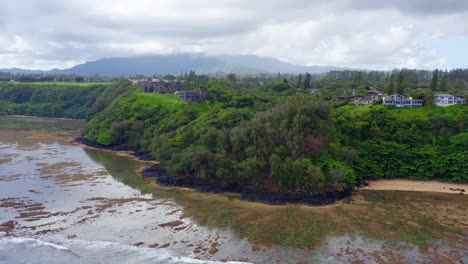 4k aerial of sea lodge beach showing dark lava rock formations, bright coral reefs, and clear turquoise water. natural textures and shallow depth highlight kauai’s untouched shoreline