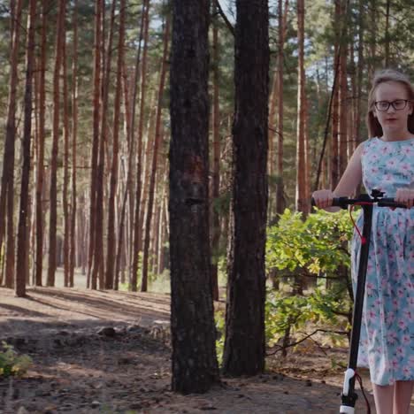 A-child-in-a-blue-summer-dress-rides-a-scooter-through-the-park-1