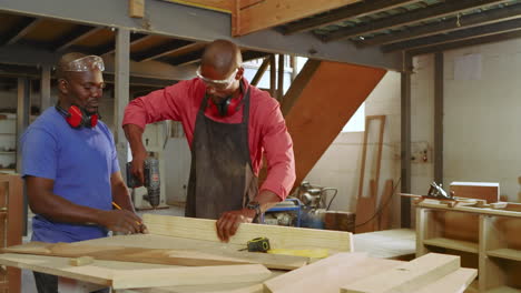 picking up pencil, african american mentor guiding trainee measuring and drilling plank at workshop