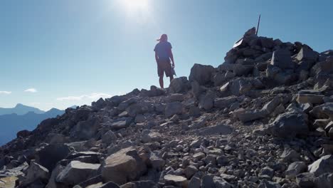 Hiker-in-the-breeze-on-peak-watching-Rocky-Mountain-range-forests-and-lakes-Reveal-Kananaskis-British-Columbia-Canada