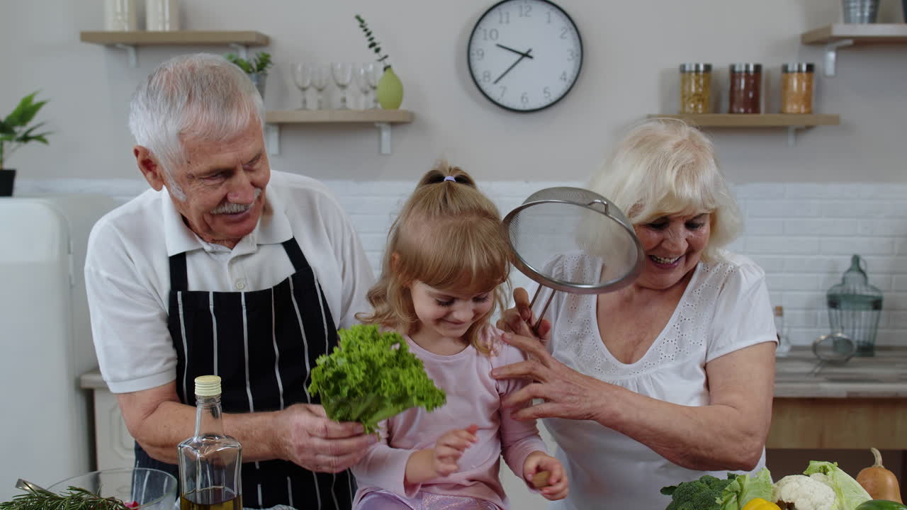 Senior woman and man with grandchild girl fooling around with strainer and vegetables at home