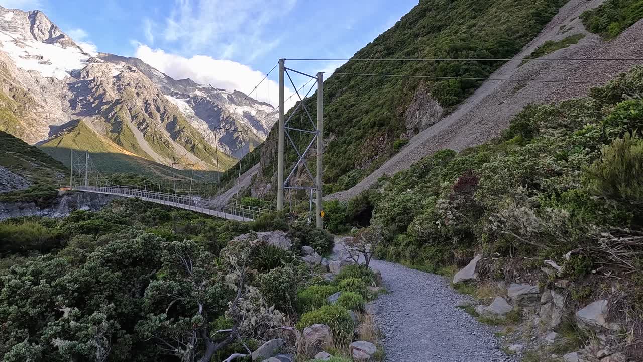 Woman walking across a suspension bridge along the Hooker Valley Trail in New Zealand. There are 3 suspension bridges in total along this popular hiking trail
