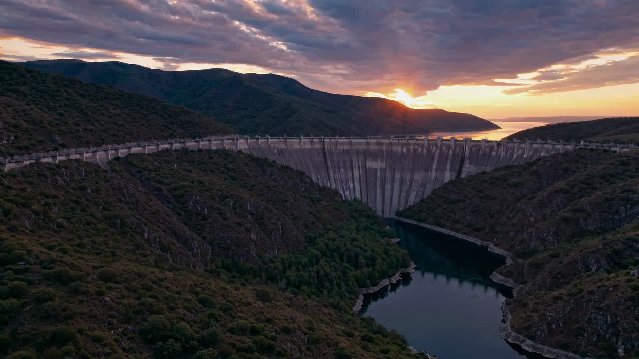 Aerial view of a dam at sunset, with dramatic clouds and vibrant colors, capturing a cinematic