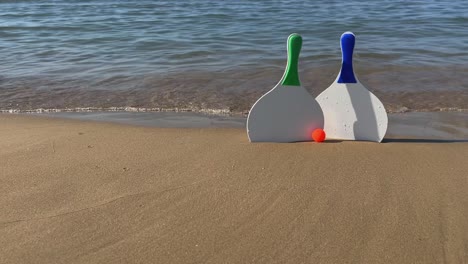 raquetas de pádel de tenis de playa y pelotas rojas en la playa de arena con olas rompiendo en la orilla
