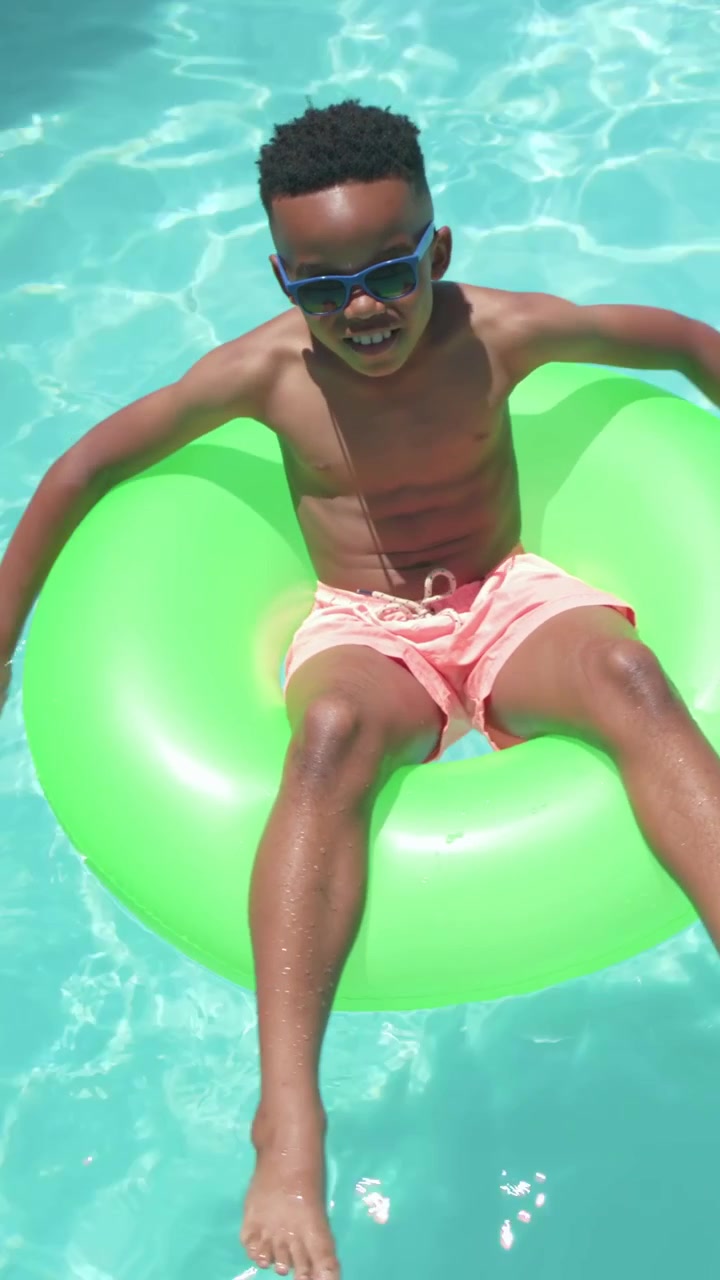 Vertical video: Weight shift causing boy steadying on ring at pool to float, wearing trunks, shades