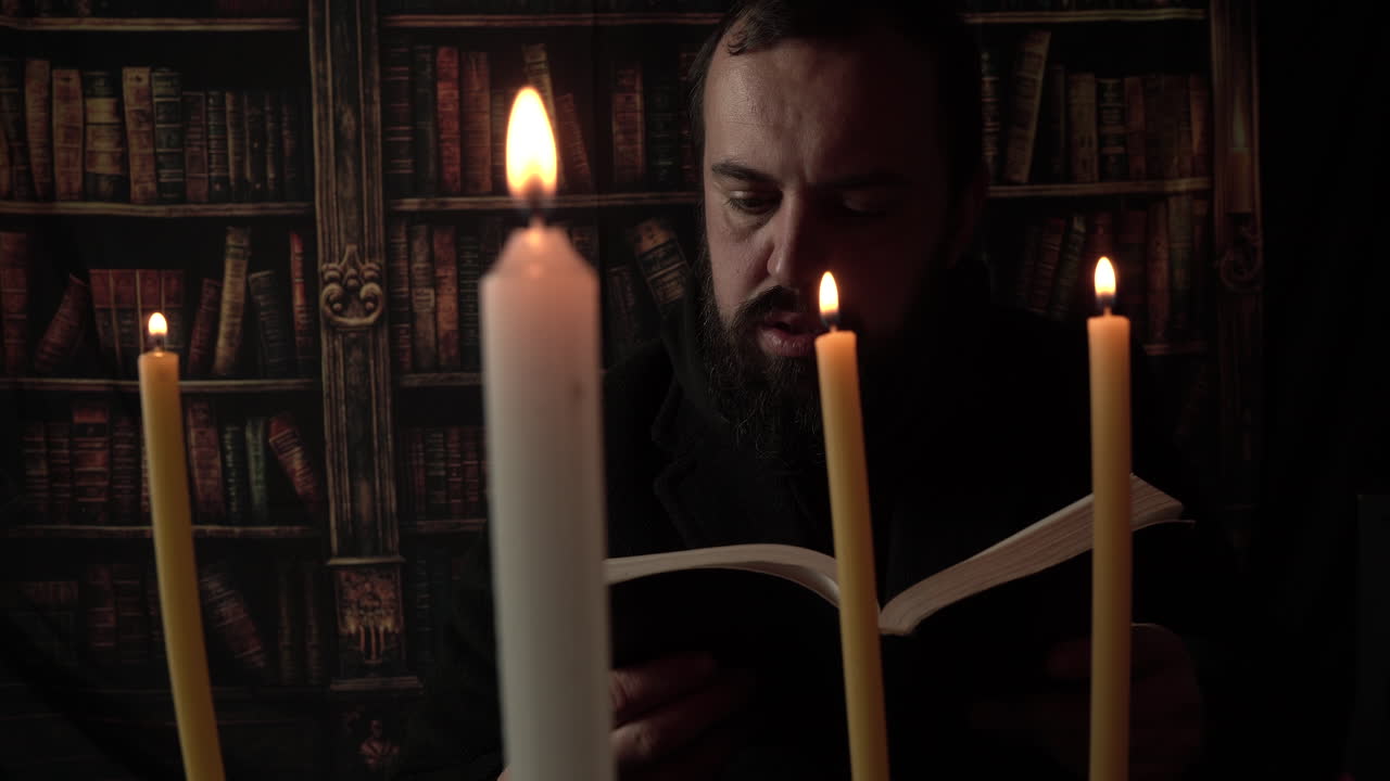 Uomo medievale che legge un libro in una stanza buia alla luce di una candela.