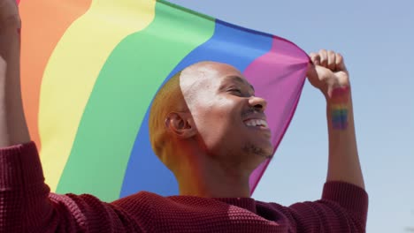 happy african american man holding lgbt rainbow flag and smiling, slow motion