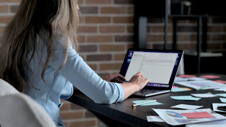Woman in blue blazer typing on a laptop at a desk in an office