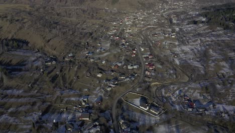 vista de drones de una pequeña comunidad agrícola en el valle debajo de una cadena montañosa bordeada de pinos y terreno cubierto de nieve