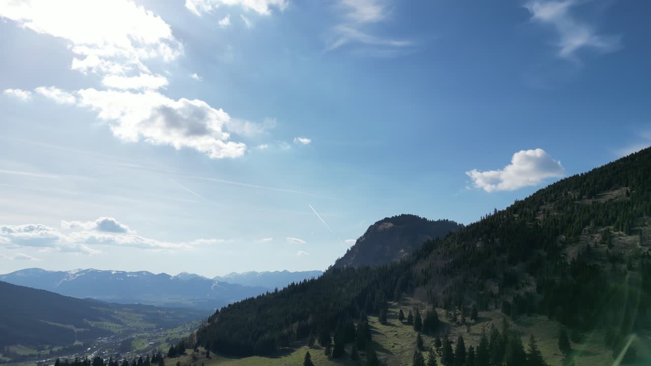 Drone view of Oberjoch in the Bavarian Alps showing snow patches, green meadows, and forested hills. A peaceful mountain village perfect for nature and travel visuals.