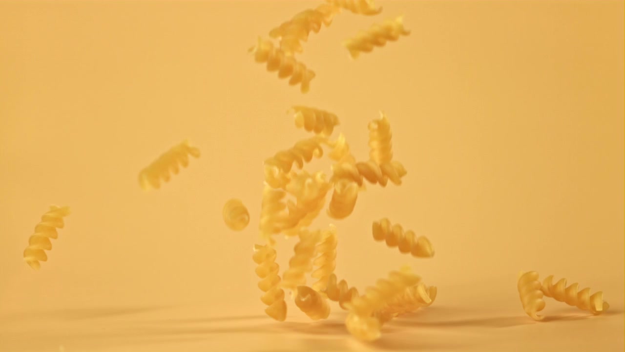 Raw Fusilli Pasta Falling in Slow Motion on Yellow Background