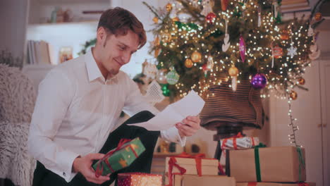 happy man holding christmas gift while reading letter at home