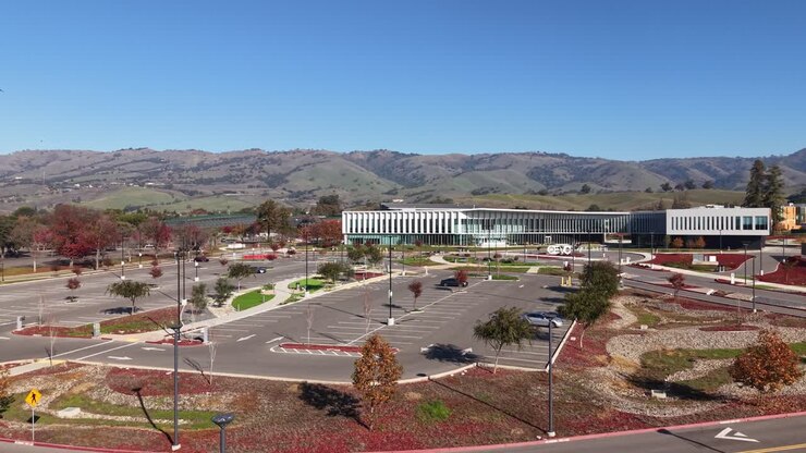 Uma visão de drone sobe acima do Evergreen Valley College, mostrando passarelas, telhados e pátios, ao mesmo tempo em que exibe o cenário da faculdade contra sopés e arredores suburbanos.
