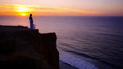 woman silhouette on cliff edge at sunset overlooking ocean