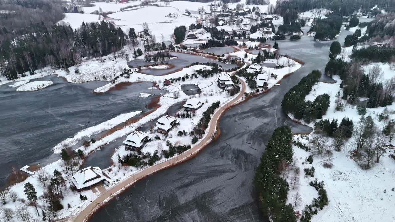Korkea panoraamailmakuva maaseudun asuinalueesta jäätyneen vesistön äärellä lumipeitteen alla