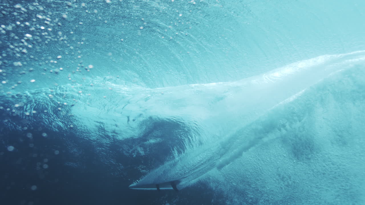 Surfer dark silhouette contrasts against barreling vortex wave, rearview slow motion