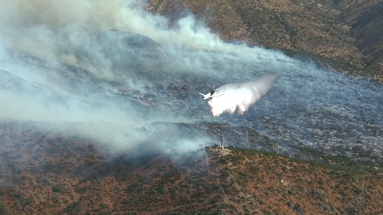 Avión de extinción de incendios lanza retardante sobre un incendio forestal en montañas áridas