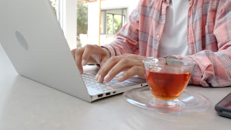 typing on laptop, man working from home with tea on table