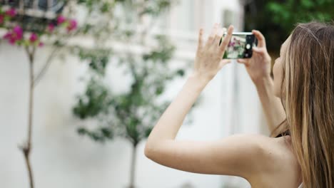 Woman-taking-mobile-photo-camera-picture-of-local-plants-and-flowers-on-the-street