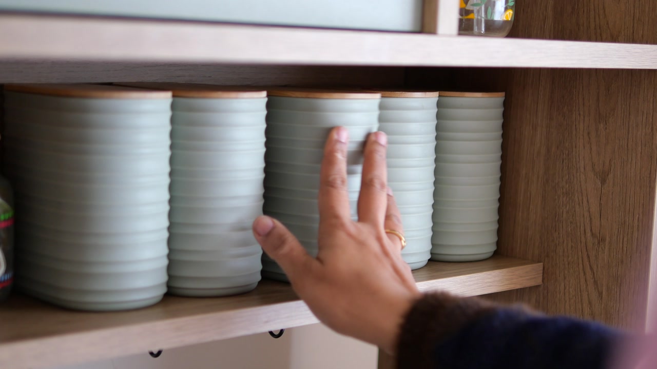 Hand taking a light green storage container from a wooden shelf
