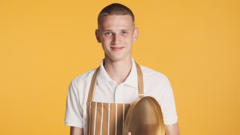 um jovem garçom sorridente com uma bandeja dourada.