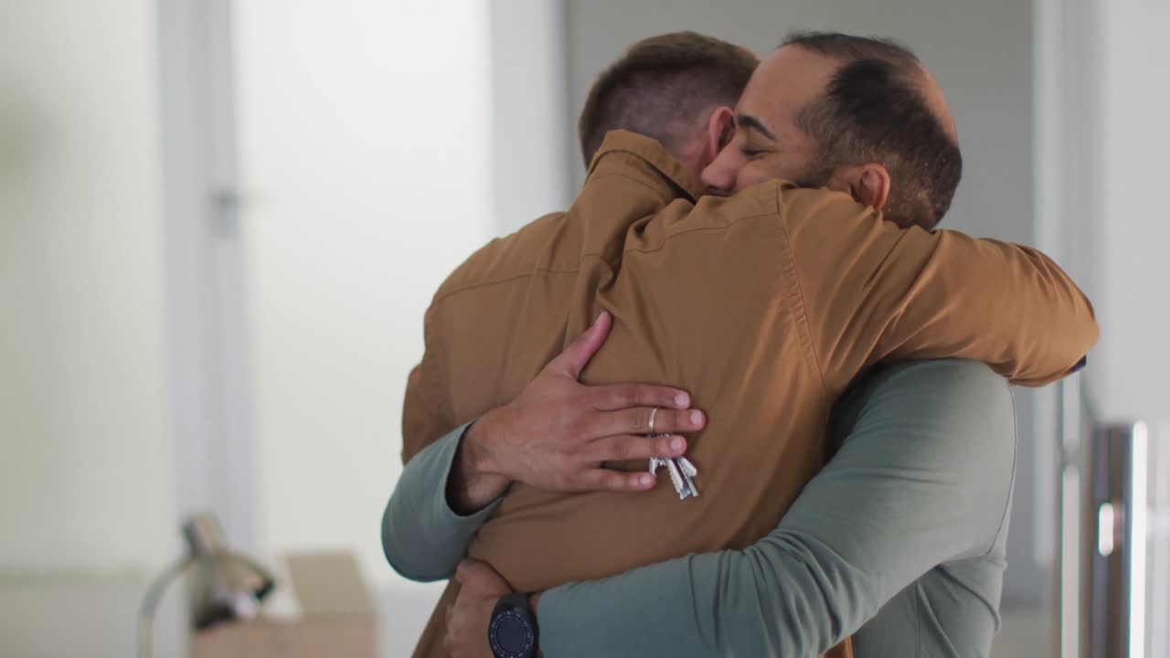 Coppia gay maschile multietnica che si abbraccia, con uno che tiene le chiavi di casa.