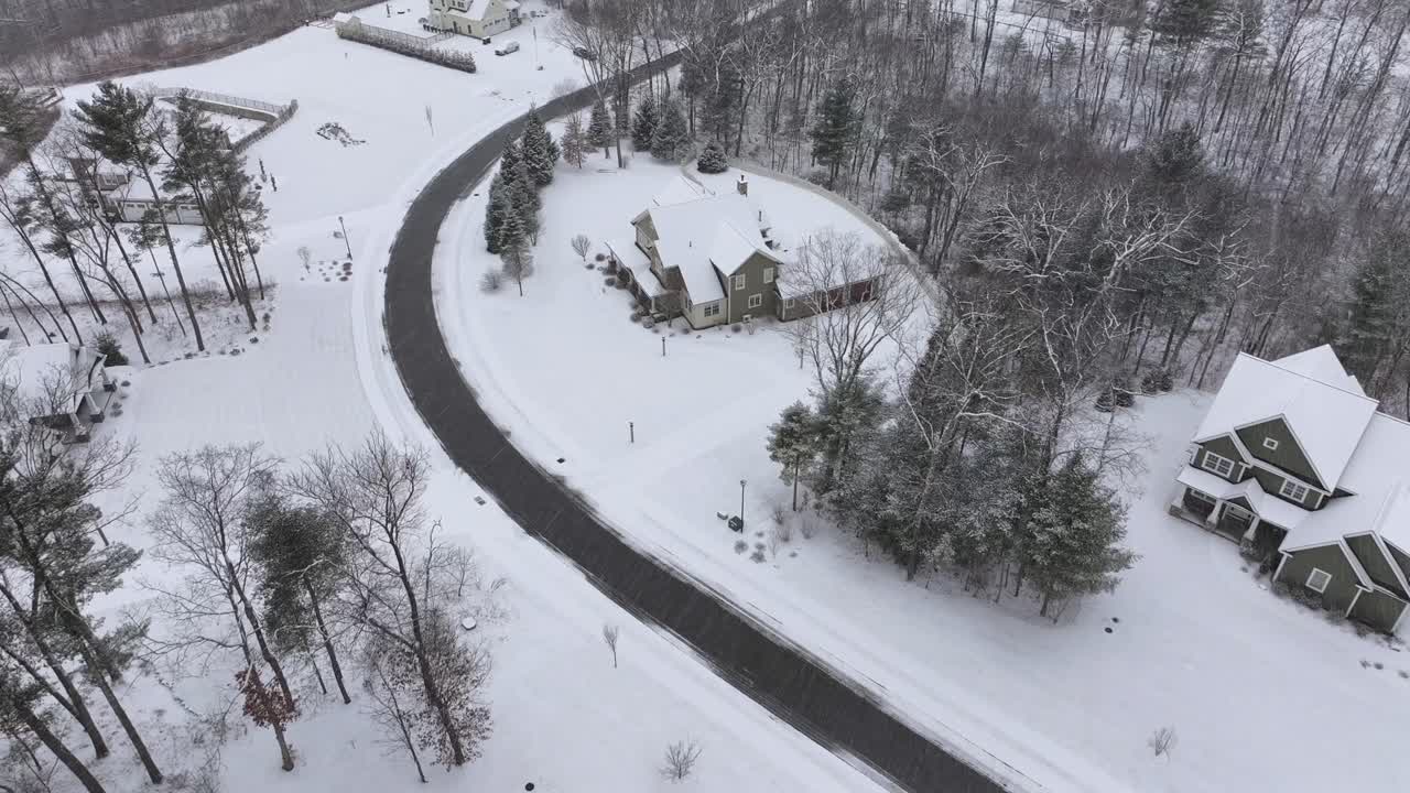Snowfall and snowflakes in suburb of american neighborhood with snow-covered houses and homes. Aerial top down shot. Conifer trees in winter.