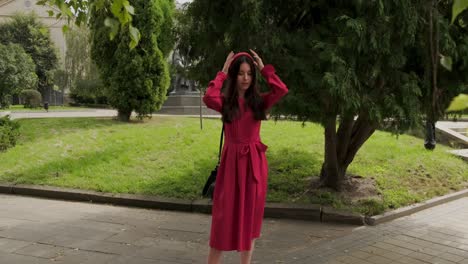 pleasing girl near trees touches hair and smiles