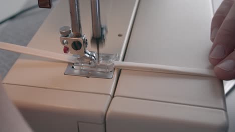 una vista de primer plano de una aguja en una máquina de coser cosiendo rápidamente una banda para una máscara facial
