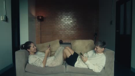 two women relaxing on a couch with smartphones