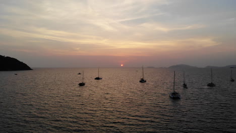 Flight-over-the-ocean-and-boat-with-sunset-and-mountains-in-the-background