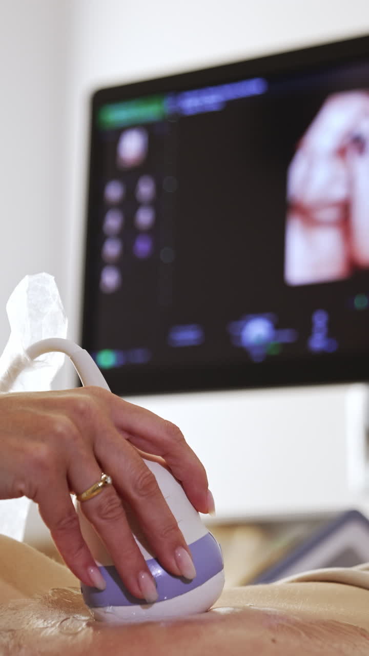 Ultrasound transducer in the doctor's hand moving by the belly. Black screen with baby image at backdrop in blur.