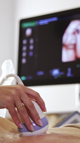 ultrasound transducer in the doctor's hand moving by the belly. black screen with baby image at backdrop in blur.