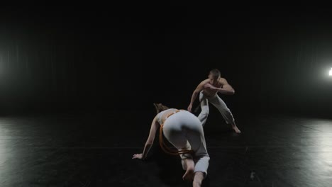 un grupo de bailarines profesionales están practicando capoeira en la oscuridad contra un foco de luz en un fondo negro de estudio. arte marcial afro-brasileño que combina elementos de la danza.