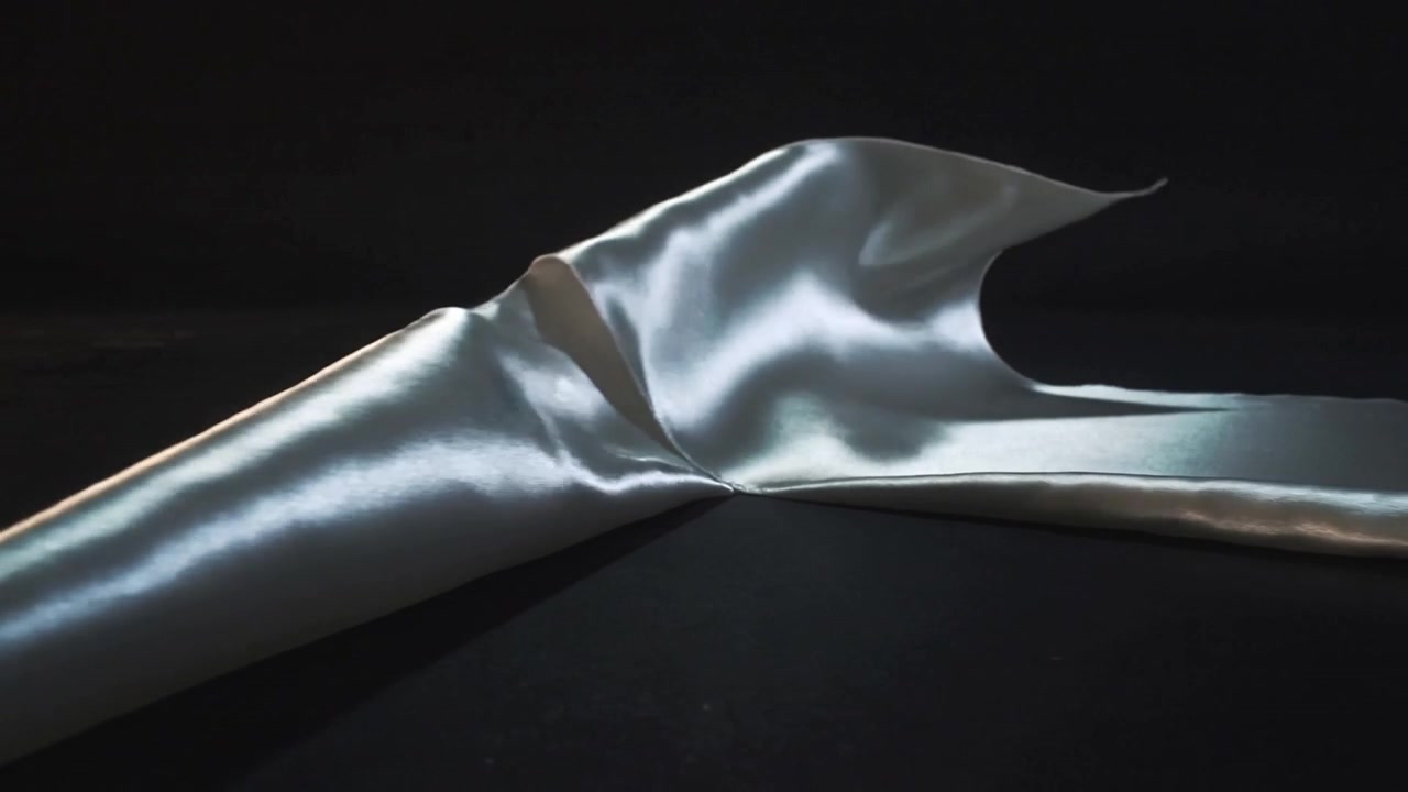 Sollevamento di un piccolo elevatore destro, con una fascia argentata che si avvolge su un tessuto nero opaco, le luci dello studio mostrano una lucentezza.