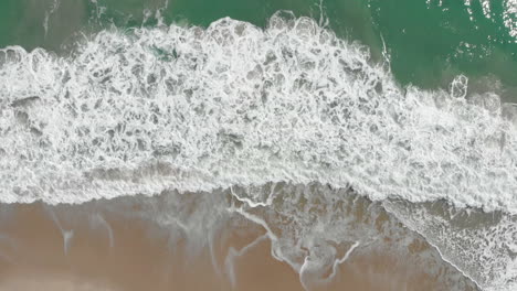 Toma-Aérea-De-Arriba-Hacia-Abajo-De-Las-Olas-Del-Océano-Salpicando-Y-La-Playa-En-La-Costa-Dorada