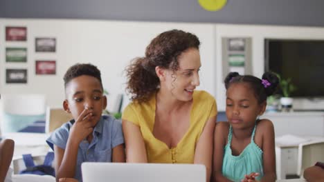 video of happy caucasian female teacher and african american pupils using laptop