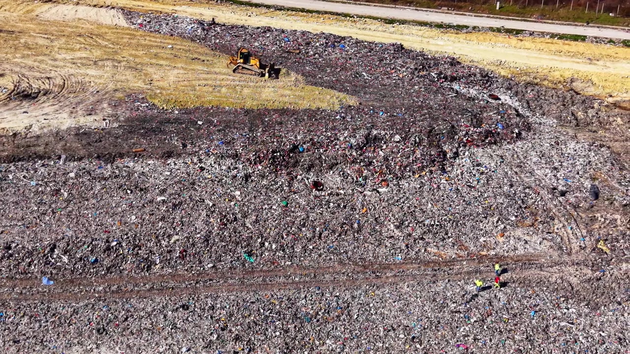 Industrial waste landfill from above. Overhead aerial view of garbage dump mound with earthmover machinery under bright sun.