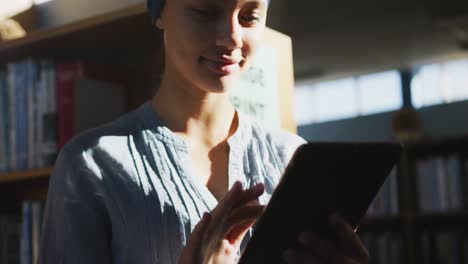 Asian-female-student-wearing-a-blue-hijab-standing-and-using-tablet