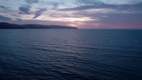 twilight hues over calm sea with distant mountains under a serene sky, aerial view