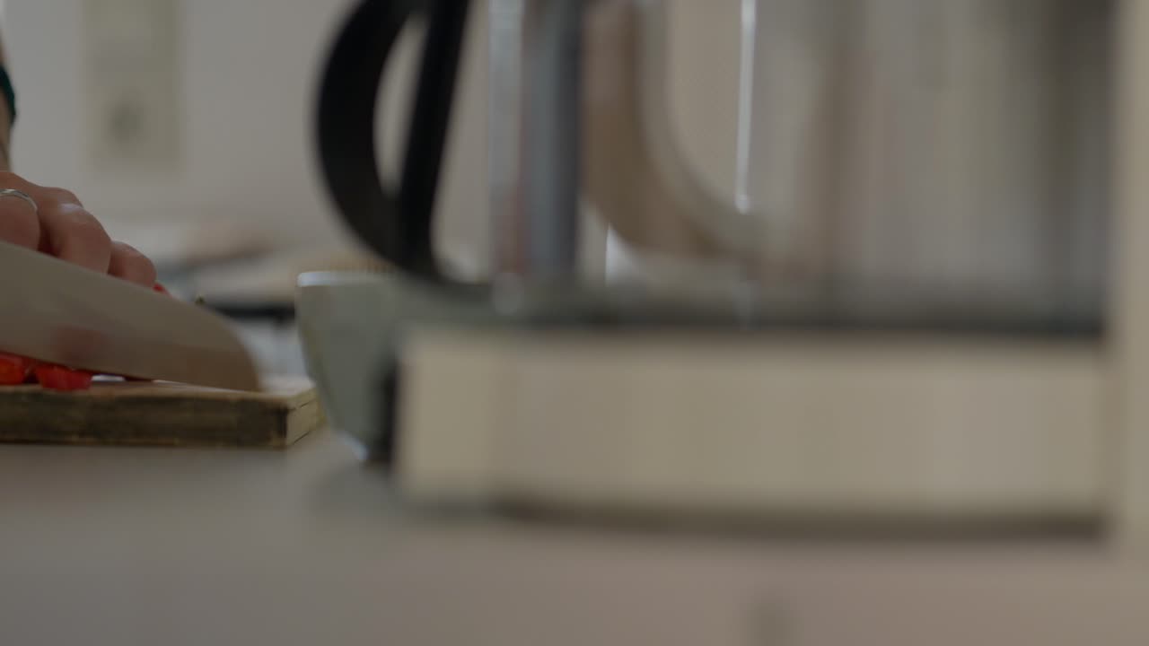 cerca de una mujer cortando un pimiento rojo con un cuchillo de chef en una pequeña cocina