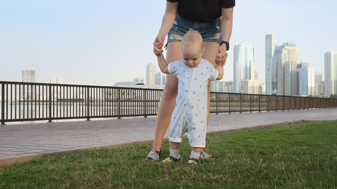 un niño sonriente sosteniendo la mano de su madre hace los primeros pasos caminando por el paseo marítimo en verano.