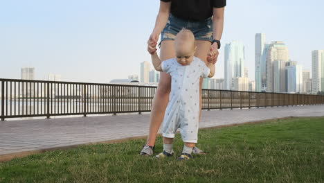 Smiling-Boy-holding-his-mother's-hand-makes-the-first-steps-walking-along-the-promenade-in-the-summer.