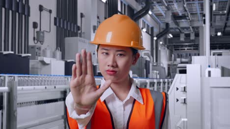 close up of asian female engineer with safety helmet disapproving with no hand sign with water production in bottling factory