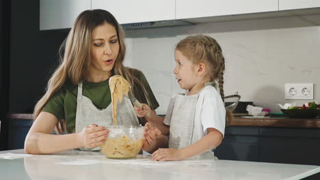 surprised girl looks at whisk with dough with mom at table