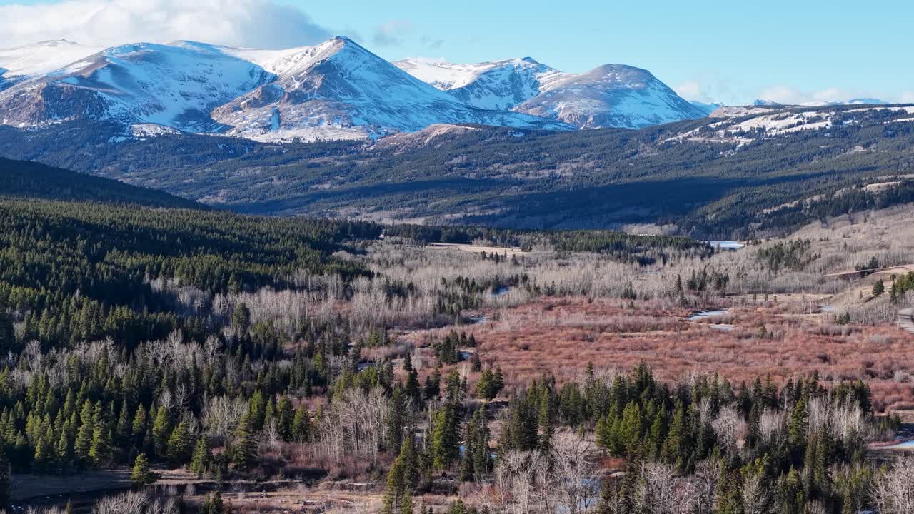 Vidsträckt flygbild över snötäckta berg och klippiga toppar som reser sig över en oländig dal med städsegröna skogar och böljande kullar i Montana