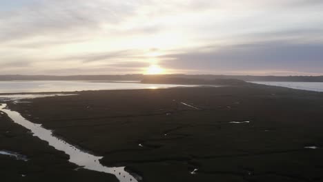 ethereal dawn sunrise aerial flyover: low grassy tidal mudflat estuary