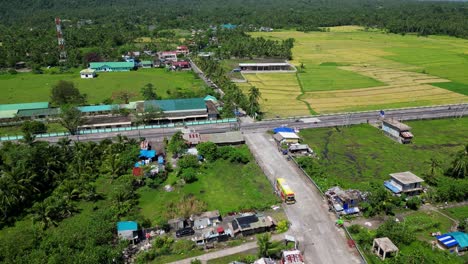 aerial approach to malilipot road curving through fields and houses, green hills in background, establishing philippines countryside
